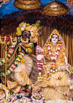 two people dressed in costumes standing next to each other with flowers on the floor and decorations around them