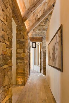 the hallway is lined with stone walls and wooden beams, along with wood flooring