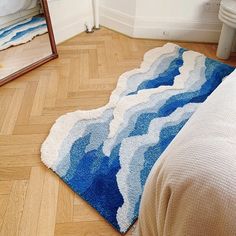 a blue rug on the floor in front of a mirror and bed with a white comforter