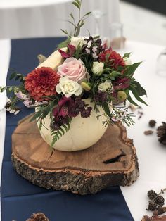 a vase filled with flowers sitting on top of a wooden slice next to a blue table cloth