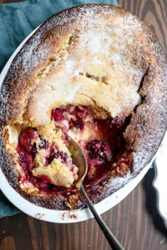 a berry cobbler in a white bowl with a serving spoon and blue napkin next to it