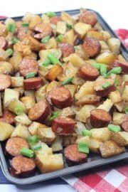 a pan filled with potatoes and sausages on top of a checkered table cloth