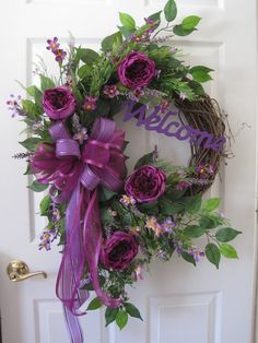 a wreath with purple flowers and green leaves on the front door is adorned with a purple ribbon