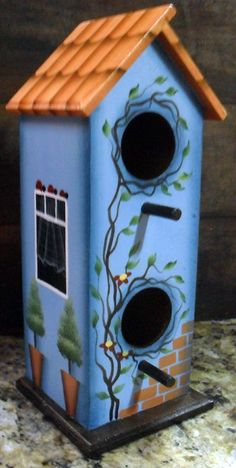 a blue birdhouse with trees painted on it's side and two holes in the roof