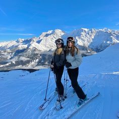 two people on skis posing for a photo in the snow with mountains in the background