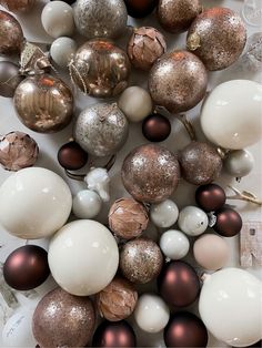 an assortment of christmas balls and ornaments on a white tablecloth with silver, brown and gold decorations