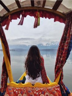 a woman sitting in a boat looking out over the water with mountains in the background