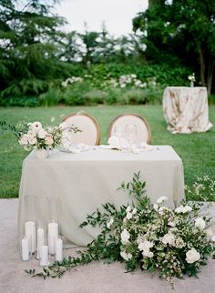 the table is set with white flowers and candles for an elegant wedding reception in the garden