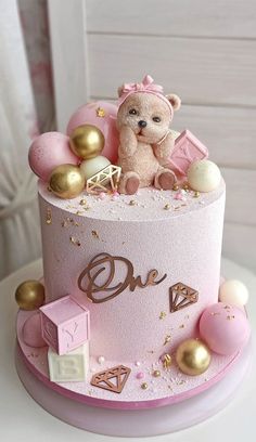 a pink and gold birthday cake with a teddy bear on top, surrounded by other decorations