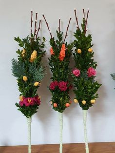 three tall vases with flowers and greenery in them sitting on a wooden table