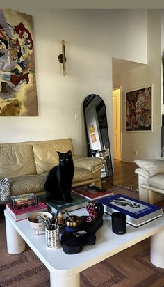 a black cat sitting on top of a white table in a living room next to a couch