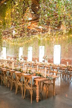 an indoor venue with tables and chairs covered in greenery, hanging from the ceiling