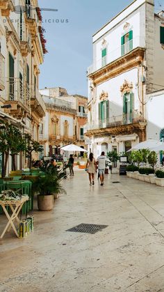 people are walking around in an old european town square with tables and chairs on the sidewalk