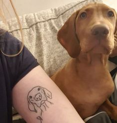 a dog is sitting next to a woman's arm with a tattoo on it