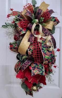 a red and green christmas wreath hanging on the front door with gold ribbon, evergreens and bells