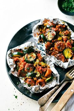 two foil packets filled with food on top of a black plate next to silverware