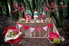 a table topped with lots of candy and flowers next to trees in the woods on a forest floor