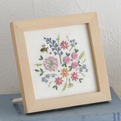 a cross stitch picture frame with flowers and a bee in it on top of some books