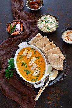 a bowl of soup with pita bread on the side and bowls of other food