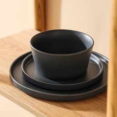 a black bowl and plate sitting on top of a wooden table next to each other