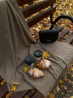 some croissants are sitting on a bench covered with a blanket and coffee cups