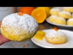 a person holding up a powdered sugar doughnut in front of some oranges