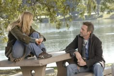 a man and woman sitting on a park bench next to each other looking at each other