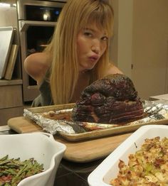 a woman sitting in front of a roasting pan filled with meat and veggies