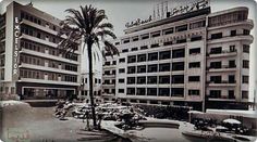 an old black and white photo of a building with palm trees in the foreground