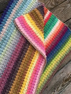 a multicolored crocheted blanket laying on top of a wooden floor next to a piece of wood