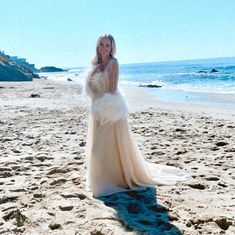 a woman standing on top of a sandy beach next to the ocean wearing a white dress