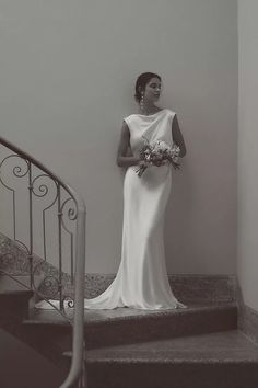 a woman in a white dress standing on some stairs with flowers and holding a bouquet