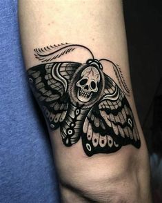 a black and white moth tattoo on the left arm, with a skull in the middle