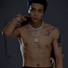 a shirtless young man with tattoos on his chest and necklaces around his neck