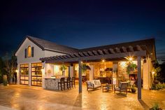 an outdoor living area at night with lights on the patio and covered dining room in the background