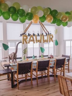 a dinosaur birthday party decoration with balloons and decorations on the ceiling, in front of a table