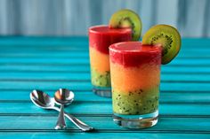 two glasses filled with fruit and kiwi slices on top of a blue wooden table