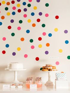 a table topped with cakes and cupcakes next to a wall covered in multicolored polka dots