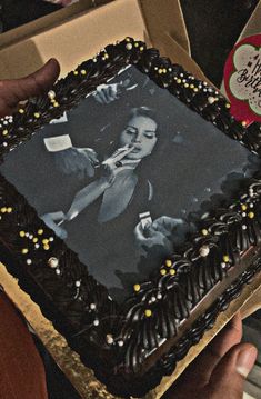 a person holding up a cake with an image on it in front of a box