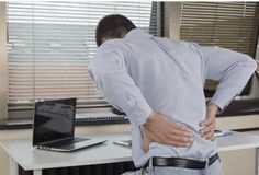 a man is holding his back in front of a laptop