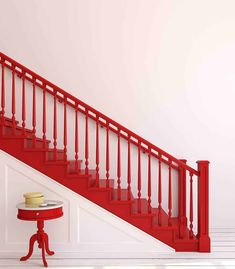 a red table with a cake on it next to a stair case in a white room