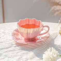 a pink tea cup sitting on top of a saucer next to a white flower