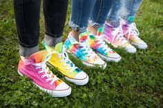 four people standing in the grass wearing colorful converses with their legs crossed and feet up