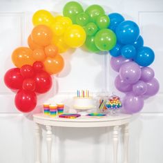 a birthday cake and balloons on a table in front of a rainbow arch with candles