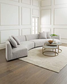 a living room with white walls and wood flooring, a round coffee table on top of a rug