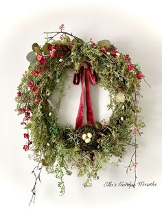 a green wreath with red ribbon hanging on the wall, decorated with flowers and greenery