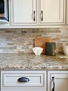 a kitchen with white cabinets and granite counter tops, including a wooden cutting board on the left side of the cabinet