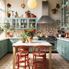 a kitchen with blue cabinets and red chairs in front of an island table surrounded by potted plants