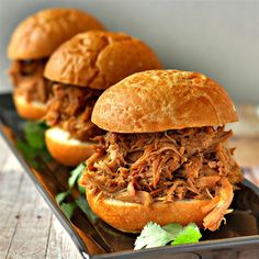 two pulled pork sandwiches sitting on top of a black plate next to some cilantro