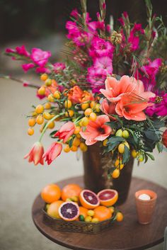 a vase filled with flowers and fruit on top of a table next to a candle